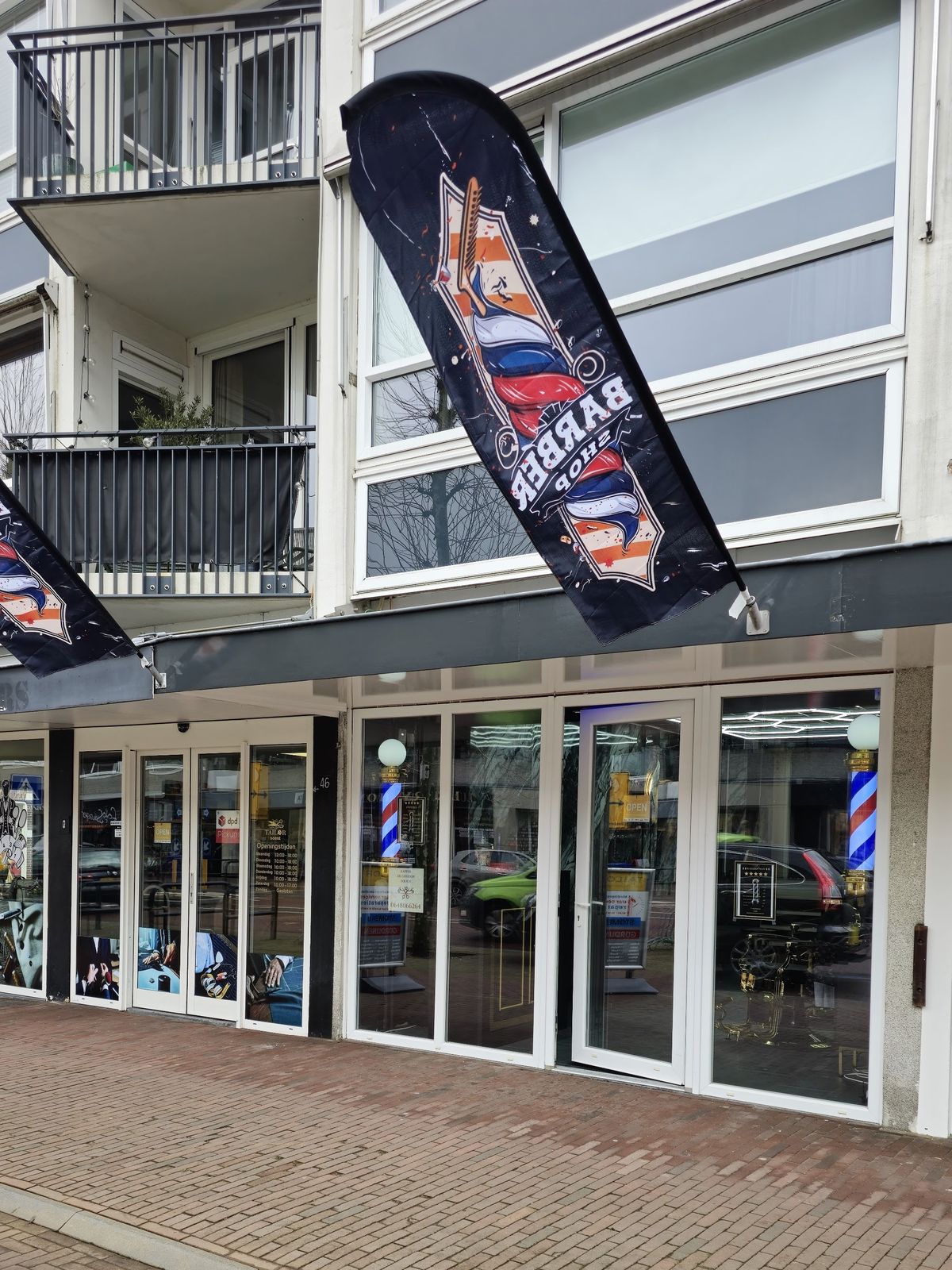 De winkelpui van De Gouden Touch aan de Van Weedestraat, met barbierspalen achter de ramen en een barbershop-vlag