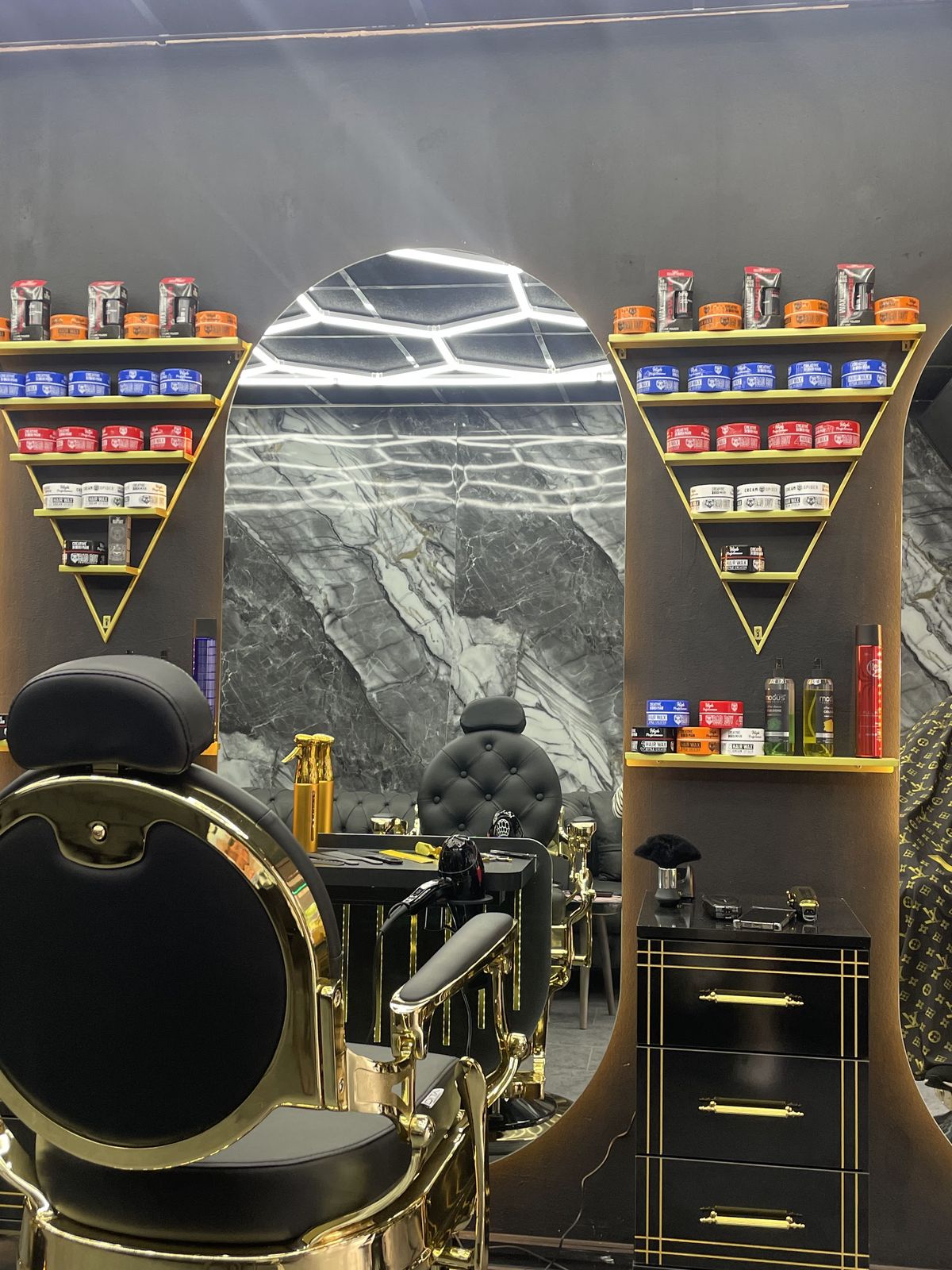 Gouden barbierstoelen voor de spiegels, met producten in de driehoekige gouden wandkasten