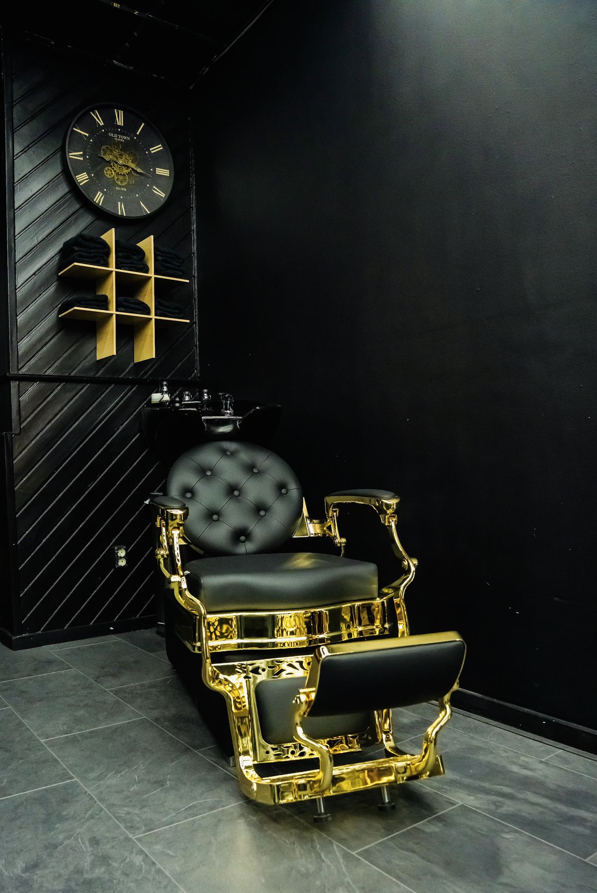 Een zwart-gouden barbierstoel voor een donkere wand met een klok